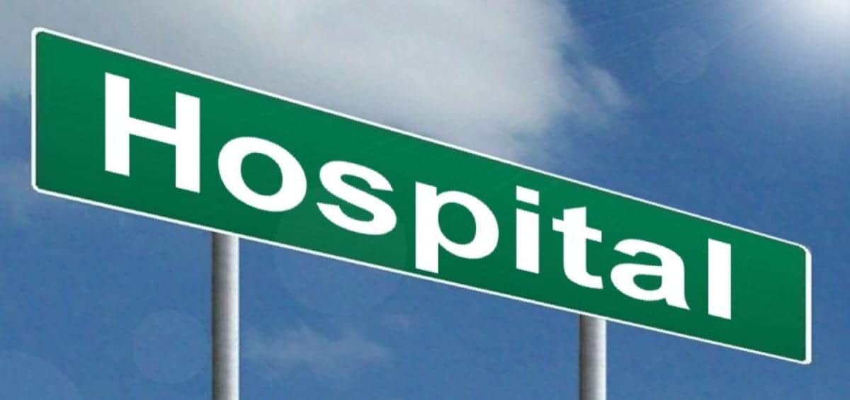 A green direction sign with the word "Hospital" written in white capital letters stands against a blue sky with a few clouds.