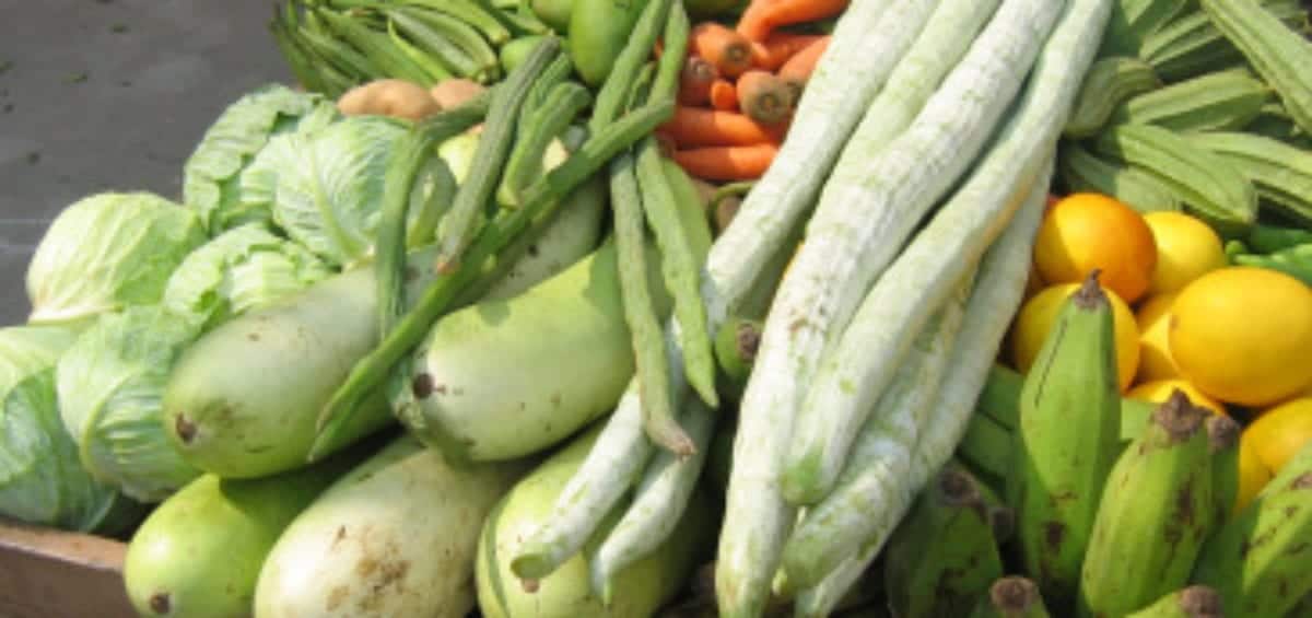 A cart displaying a variety of fresh vegetables including cabbages, carrots, long white gourds, okra, bananas, and other produce.