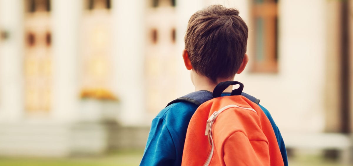 Boy with backpack in front of a school building.