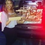 Ready to deliver A woman stands next to an open car trunk filled with bakery boxes, holding one such box and smiling at the camera.