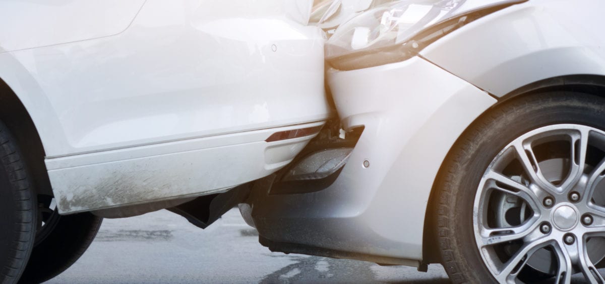 A rear-end collision between a silver car and a white SUV. The front bumper of the silver car is crumpled, and it is impacting the rear bumper of the white SUV.