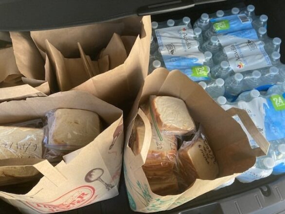 Bags filled with sandwiches and a pack of bottled water are placed in the trunk of a vehicle.