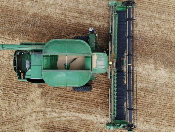 Aerial view of a green combine harvester in a harvested field, showing the machine from above with visible crop rows below.